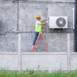 addetto su una scala con dispositivi di sicurezza che controlla il motore di un condizionatore